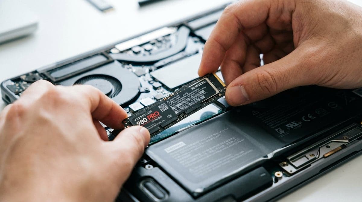 노트북 내부에 M.2 NVMe SSD를 장착하는 모습, 슬롯에 SSD를 비스듬히 삽입하고 있는 손이 보인다